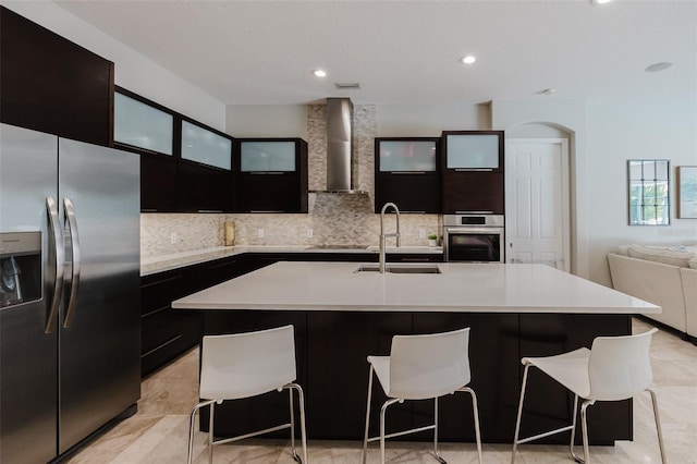 kitchen with a sink, stainless steel appliances, light countertops, wall chimney exhaust hood, and modern cabinets