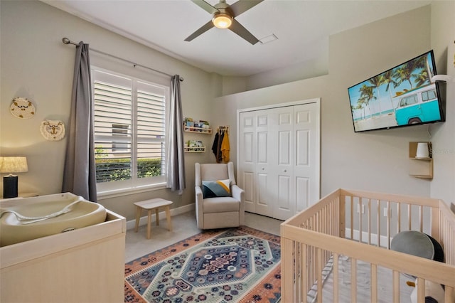 carpeted bedroom featuring a nursery area, baseboards, a closet, and ceiling fan