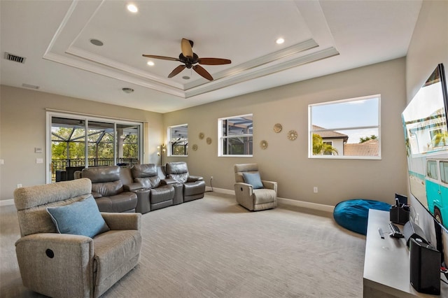 living room featuring a raised ceiling, carpet flooring, a ceiling fan, and visible vents