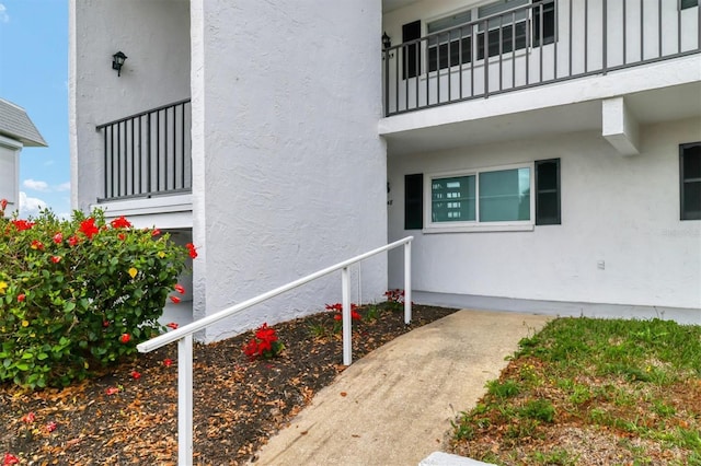 view of exterior entry with a balcony, board and batten siding, and stucco siding