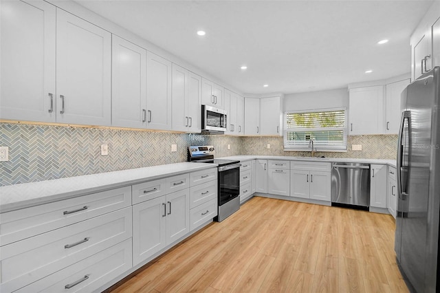 kitchen with light wood finished floors, a sink, decorative backsplash, white cabinets, and appliances with stainless steel finishes