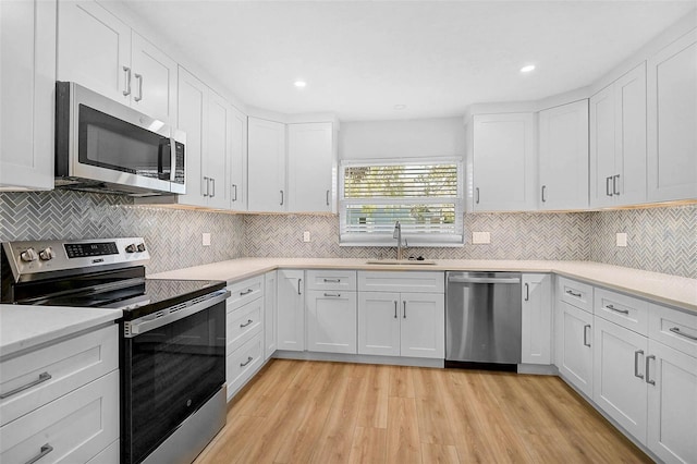 kitchen with light countertops, appliances with stainless steel finishes, light wood-style floors, white cabinets, and a sink