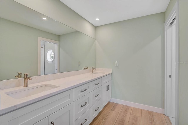 bathroom with double vanity, wood finished floors, baseboards, and a sink