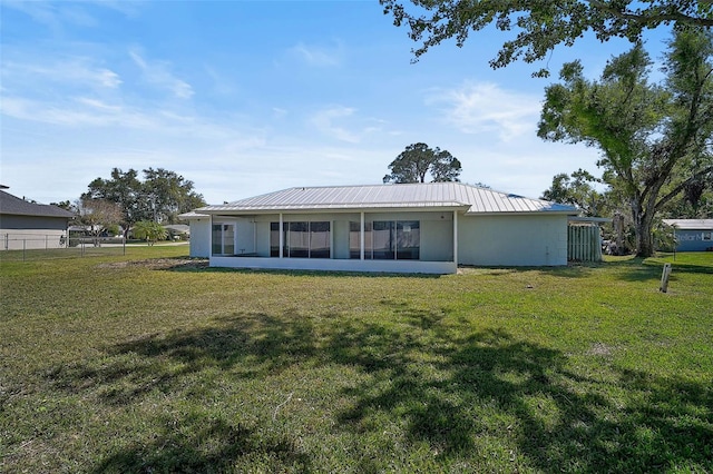 rear view of property with fence, stucco siding, metal roof, a yard, and a sunroom