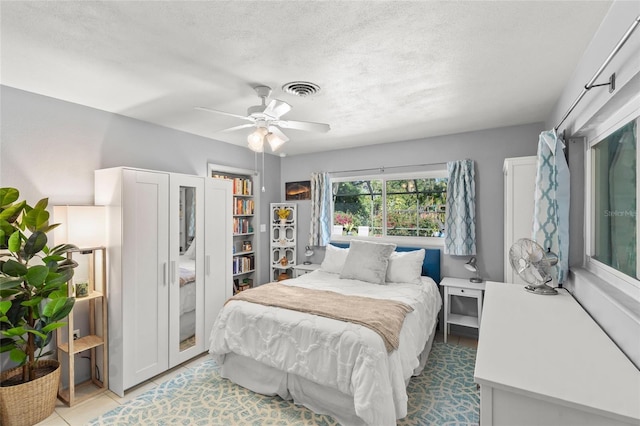 tiled bedroom featuring a ceiling fan, visible vents, and a textured ceiling