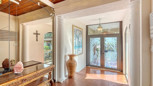 doorway to outside with a textured wall, tile patterned flooring, ornate columns, and french doors