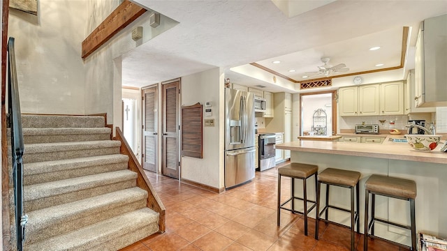 kitchen with a ceiling fan, a breakfast bar area, a peninsula, stainless steel appliances, and cream cabinetry