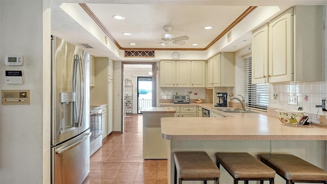 kitchen with crown molding, cream cabinets, a sink, stainless steel fridge, and a peninsula