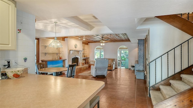 tiled living area featuring a fireplace with raised hearth, stairway, arched walkways, and a ceiling fan