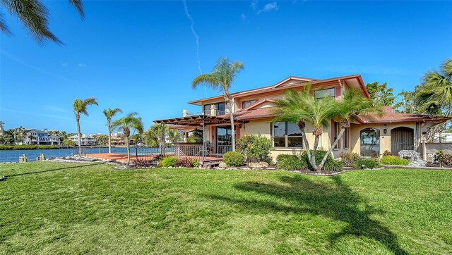 rear view of property featuring a water view, a lawn, and stucco siding