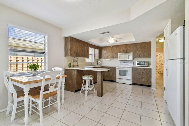 kitchen featuring white appliances, light tile patterned floors, a raised ceiling, a peninsula, and light countertops