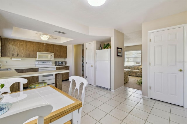 kitchen with light tile patterned floors, white appliances, a sink, light countertops, and a tray ceiling