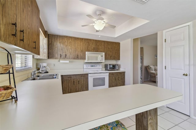 kitchen featuring a raised ceiling, light countertops, a sink, white appliances, and a peninsula