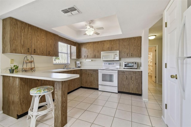 kitchen featuring a peninsula, white appliances, visible vents, light countertops, and a tray ceiling