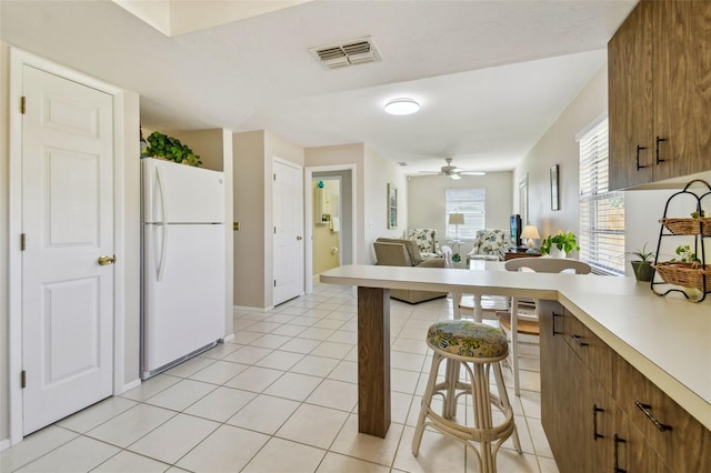 kitchen with visible vents, brown cabinetry, freestanding refrigerator, light countertops, and light tile patterned flooring