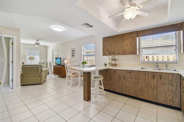 kitchen with open floor plan, a tray ceiling, light countertops, a sink, and light tile patterned flooring