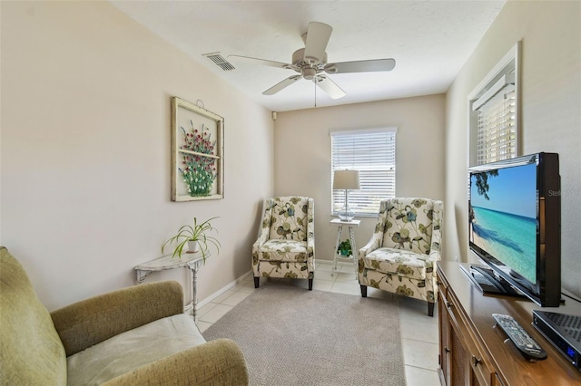 living area with light tile patterned floors, a ceiling fan, visible vents, and baseboards