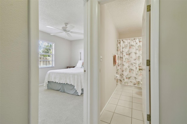 carpeted bedroom with tile patterned flooring, baseboards, ceiling fan, and a textured ceiling