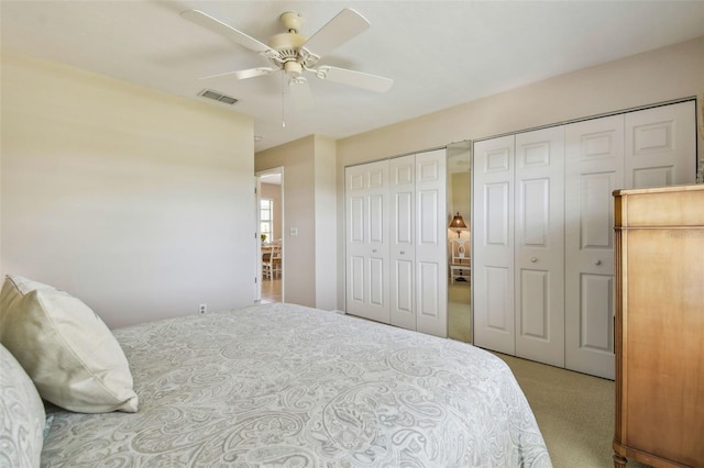 carpeted bedroom featuring visible vents, ceiling fan, and two closets