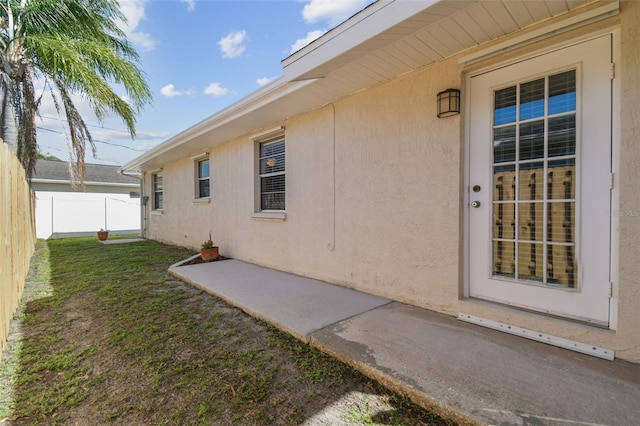 entrance to property featuring a lawn, fence, and stucco siding