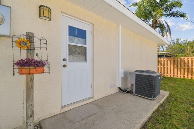 property entrance featuring cooling unit, fence, and stucco siding