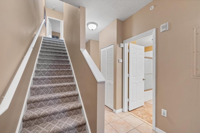 stairway with tile patterned floors, baseboards, and a textured ceiling