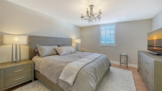 bedroom featuring an inviting chandelier, baseboards, and light wood finished floors