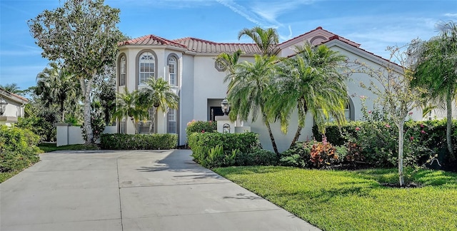 mediterranean / spanish-style home featuring a tile roof, a front lawn, driveway, and stucco siding