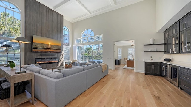 living room with baseboards, coffered ceiling, light wood-style floors, a towering ceiling, and a large fireplace