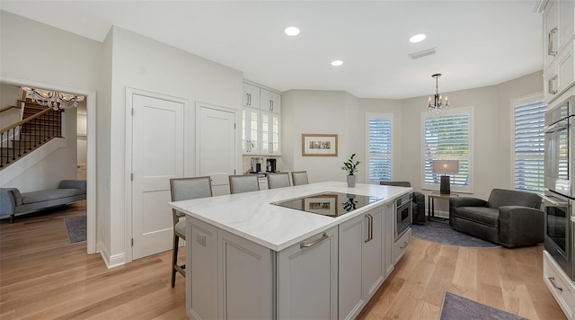 kitchen featuring an inviting chandelier, double oven, black electric cooktop, light wood-type flooring, and a center island