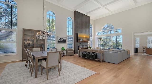 dining room featuring baseboards, coffered ceiling, a fireplace, light wood-style floors, and a notable chandelier