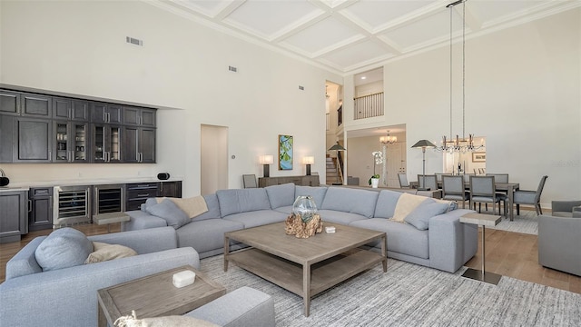 living area featuring visible vents, a notable chandelier, beverage cooler, coffered ceiling, and light wood-style floors