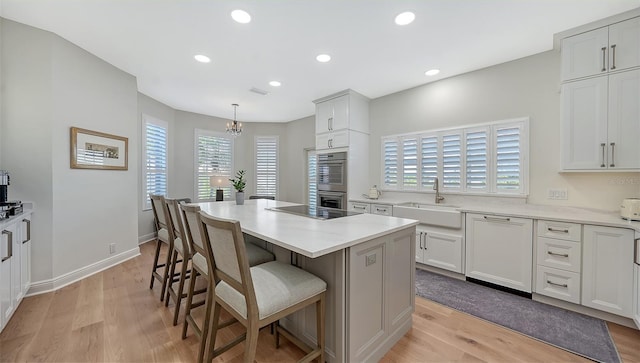 kitchen with light wood finished floors, dishwasher, a breakfast bar, stainless steel double oven, and a sink