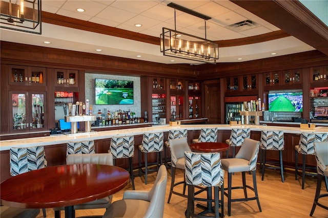 bar with a community bar, visible vents, a raised ceiling, and ornamental molding