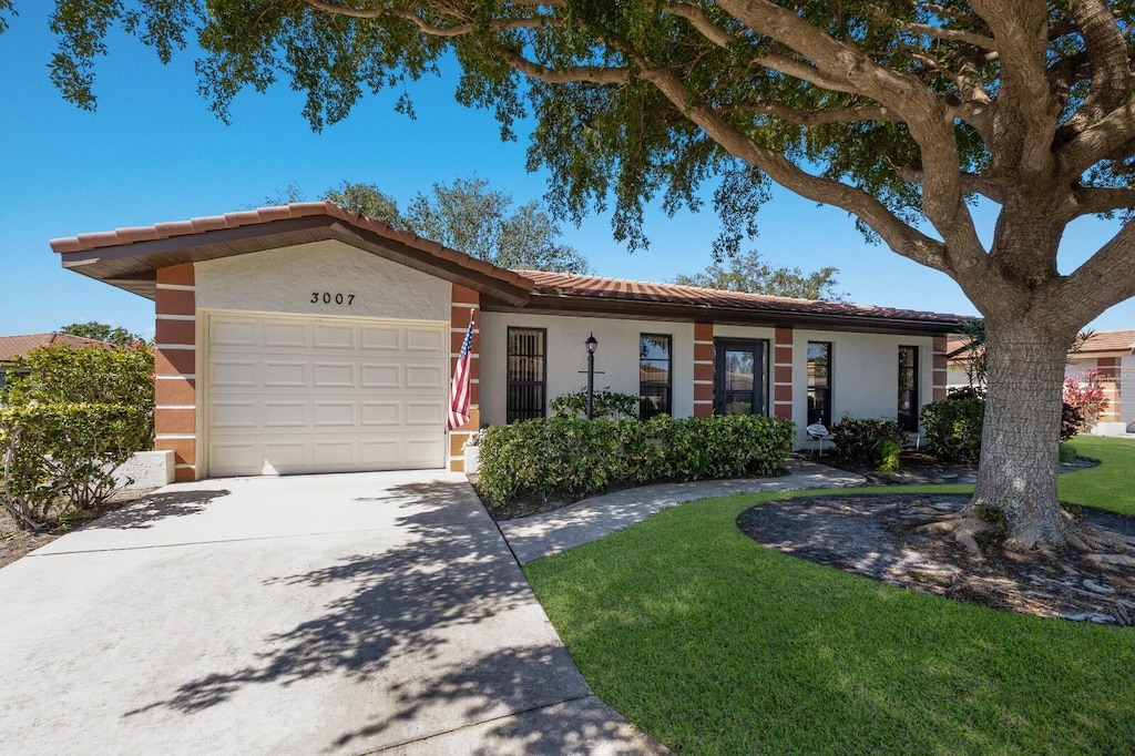 single story home with an attached garage, a tile roof, concrete driveway, stucco siding, and a front lawn