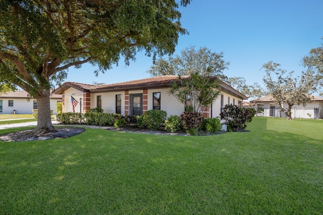 view of front facade featuring stucco siding, a tile roof, fence, and a front yard