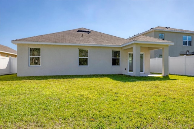 back of house with stucco siding, roof with shingles, a yard, and fence