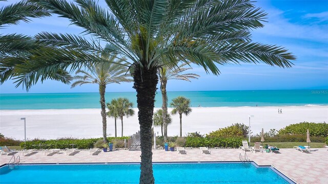 pool with a water view, a patio area, fence, and a beach view