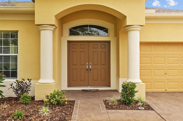 entrance to property featuring a garage, roof with shingles, and stucco siding