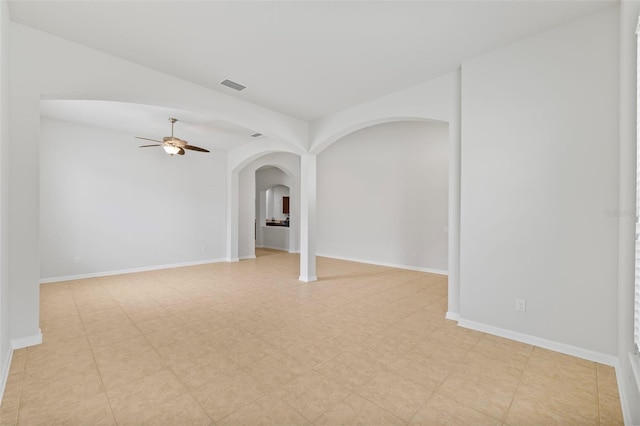 unfurnished room with ceiling fan, visible vents, arched walkways, and baseboards