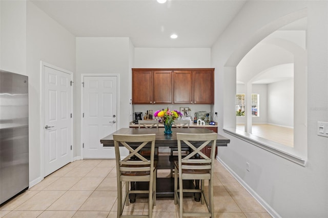 kitchen with freestanding refrigerator, arched walkways, baseboards, and light tile patterned floors