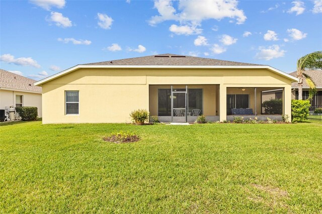 rear view of property featuring central AC unit, a lawn, a sunroom, and stucco siding