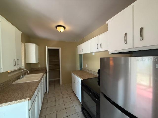 kitchen with light tile patterned floors, a sink, white cabinetry, freestanding refrigerator, and black electric range oven