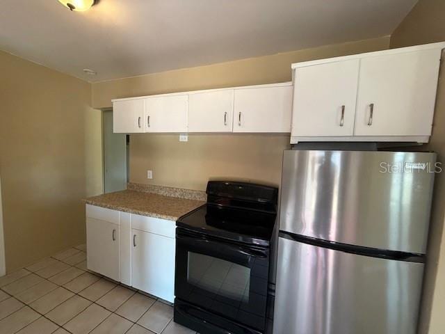 kitchen with light tile patterned floors, white cabinets, black range with electric stovetop, freestanding refrigerator, and light countertops