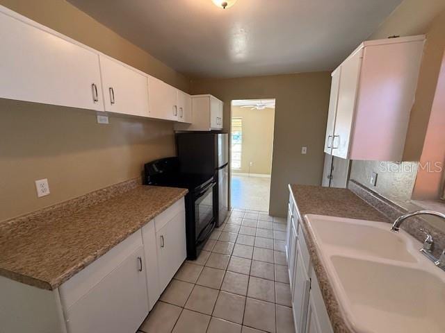 kitchen featuring light tile patterned floors, black / electric stove, a sink, white cabinetry, and a ceiling fan