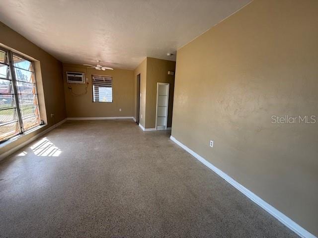 spare room featuring a ceiling fan, an AC wall unit, and baseboards