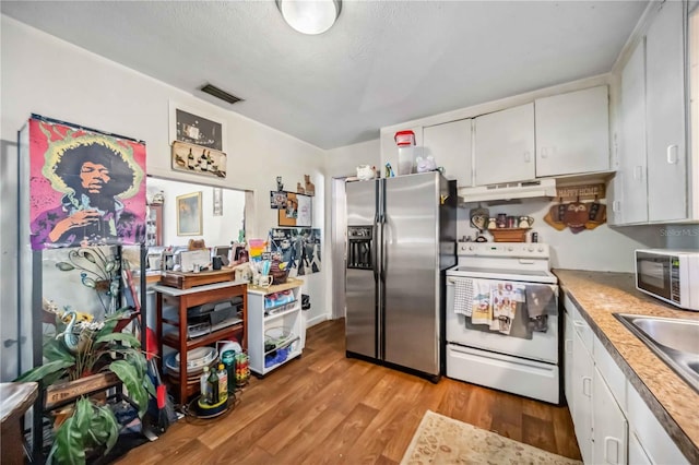 kitchen with stainless steel appliances, light countertops, white cabinetry, light wood-type flooring, and under cabinet range hood