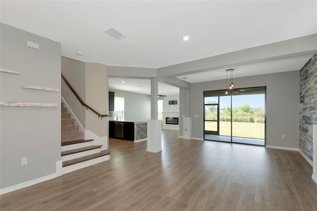 unfurnished living room featuring visible vents, wood finished floors, a glass covered fireplace, stairway, and baseboards