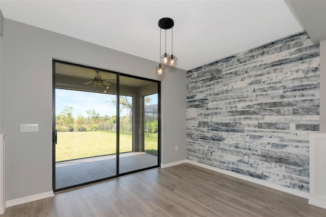 unfurnished room featuring a ceiling fan, an accent wall, baseboards, and wood finished floors