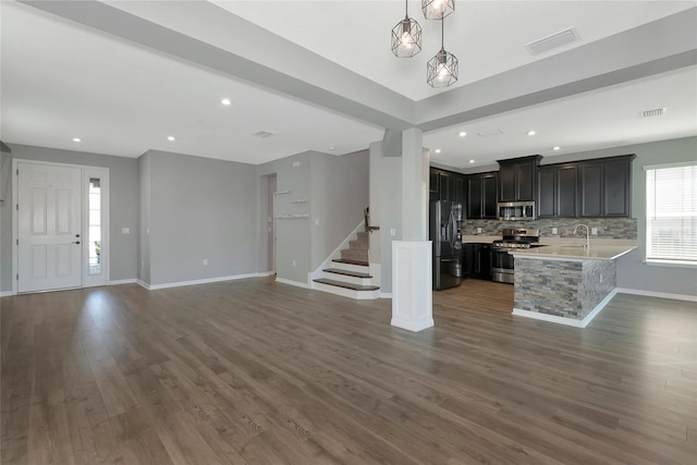 unfurnished living room featuring stairway, baseboards, visible vents, a sink, and dark wood-type flooring